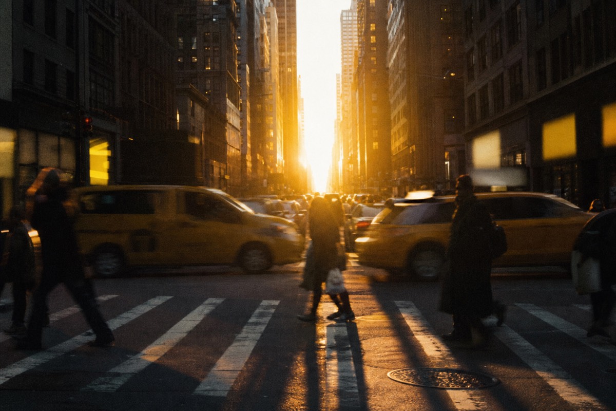 Midtown Manhattan avenue at golden hour with taxis and crosswalk crowds