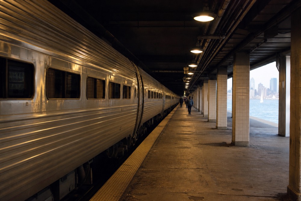 Silver intercity train carriages resting at a long underground platform, tiled columns receding into shadow, warm overhead lamps pooling light on worn concrete