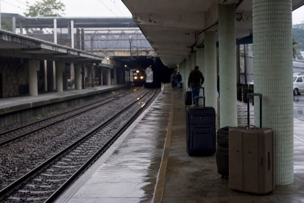 Long covered railway platform at a northeastern city station, tiled columns receding, suitcases on damp concrete, a train's headlights approaching through the dim tunnel