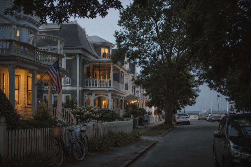 Victorian seaside houses with wraparound porches and pastel clapboard along a quiet resort street, mature shade trees, bicycles leaning against a picket fence