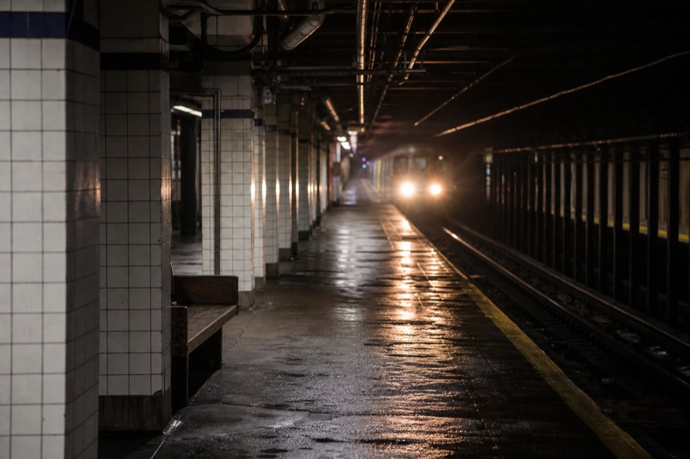 An empty subway platform at night, tiled columns receding, a single bench, headlights of an approaching train blurring the far end of the tunnel.