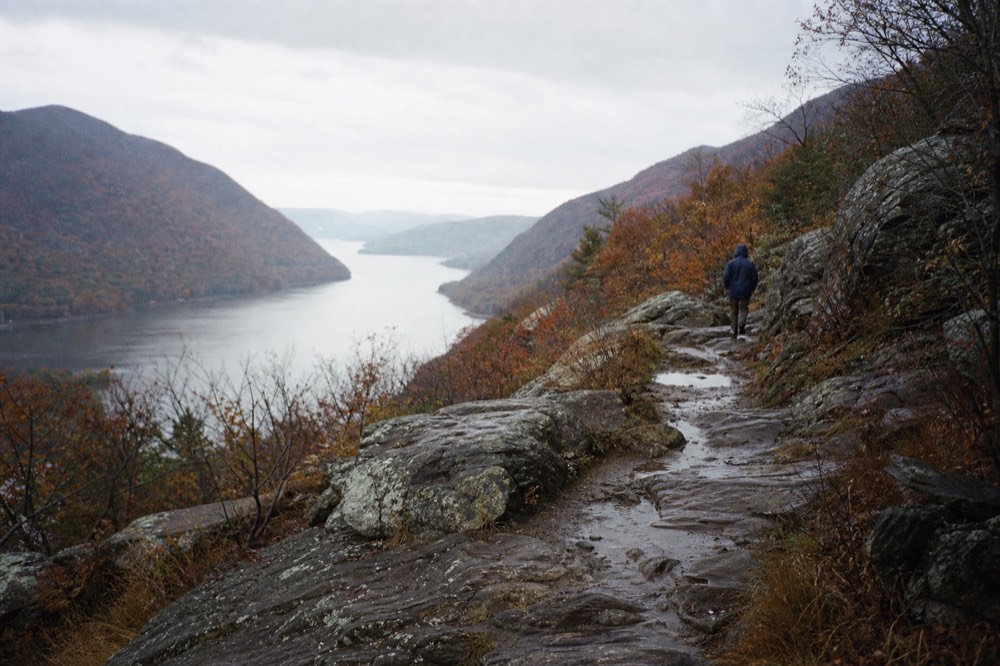 Wide river valley seen from a rocky ridge trail in October, rust and amber hillsides folding into blue distance, lichen-covered stone underfoot